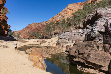 Person walking along the Waterhole Walk, wearing a backpack. Rock wall reflected on the water pound. Ormiston gorge, Macdonnell ranges, Northern Territory NT, Australia, Oceania
