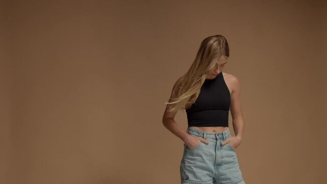 Blonde woman with long hair in studio on warm beige background with hair blowing slow motion