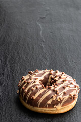 Doughnut covered with chocolate and caramel icing on black stone background