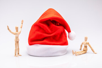 Wooden mannequins surrounding a red and white Christmas hat isolated in front of a white background