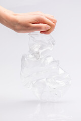 Close-up of a white people's hand crushing a crumpled plastic bottle in front of a white background