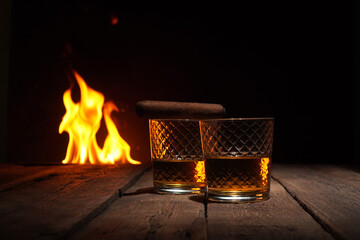 Two glasses of whiskey and cigar on a wooden table in front on a fire flame background