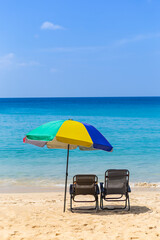 Relaxing by the beautiful beach, summer holiday, beach chair under colorful umbrella looking at blue sea ad clear blue sky