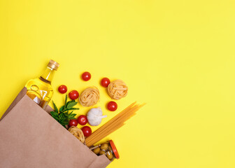 Olive oil, pasta, tagliatelle, olives, egg, cherry tomatoes, garlic in a paper bag on yellow background
