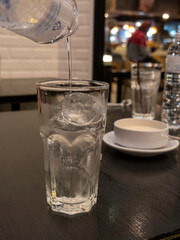 Ice cubes in a glass, 1 glass, water pouring down on the glass, placed on a black table, blur background