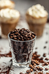 Coffee beans in a glass cup and in the background a cup with coffee and whipped cream