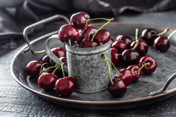 Metallic vintage tray, surface and cup with red juicy cherries inside the cup and scattered around the tray