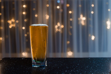 light beer in a figured glass on a black table on a blurred background
