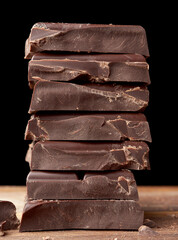 broken black chocolate on a wooden table, culinary sweet ingredient