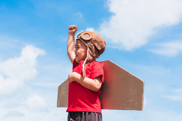 Happy Asian funny child or kid little boy smile wear pilot hat and goggles play toy cardboard airplane wing flying raises hand up against summer blue sky cloud background, Startup freedom concept © sorapop