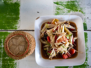 Northeastern style Spicy Papaya Salad and Vermicelli is on a white dish, next to a sticky rice...