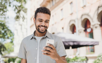 Young handsome student man using smartphone. Smiling joyful guy summer portrait. Cheerful men...