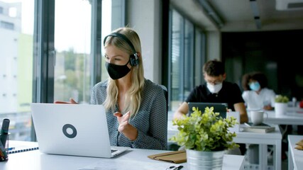 Young woman with face mask back at work in office after lockdown, having video call. - Powered by Adobe