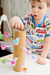 Make it at home. DIY toy for improvement of coordination, balance and fine motor skills. Kid inserting pompons into dosing teaspoons.