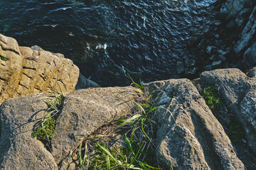 top view to the edge of a steep cliff with green grass and dark turquoise sea background on a summer day at sunset. Nature and outdoor concept.
