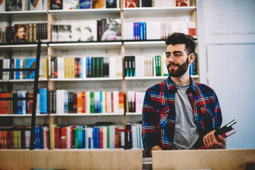Happy successful hipster guy picking literature and making research in bookstore