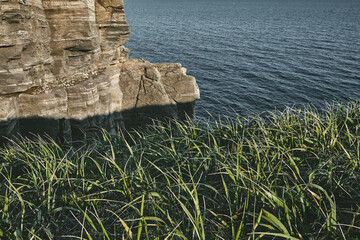 top view to the edge of a steep cliff with green grass and dark turquoise sea with rocks background on a summer day at sunset. Nature and outdoor concept.