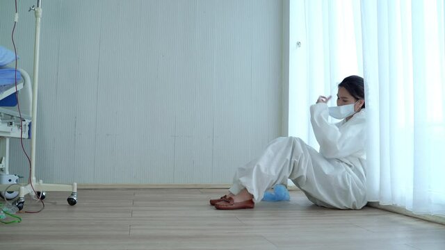 In An Epidemic Situation Covid 19, An Asian Woman Doctor Sat Down All The Way To The Ground, Removing His Mask And Headgear.The Doctor Is Very Tired, Exhausted After Working Hard.
