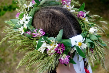 Naklejka premium Beautiful woman in wreath of midsummer flowers on heads in meadow on sunny summer day. rear view 