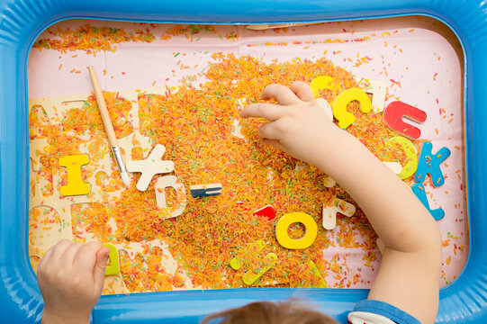 Kid learning ABC's. Early education for toddlers with colored rice as sensorial elements. Therapy for children with easy learning.