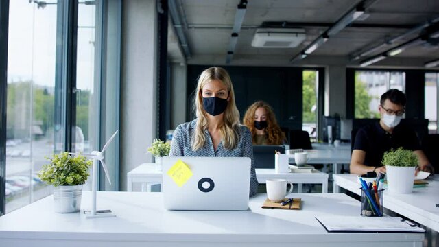 Young people with face masks back at work in office after lockdown.