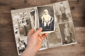 old man’s male hands hold old retro family photos over an album with vintage monochrome...