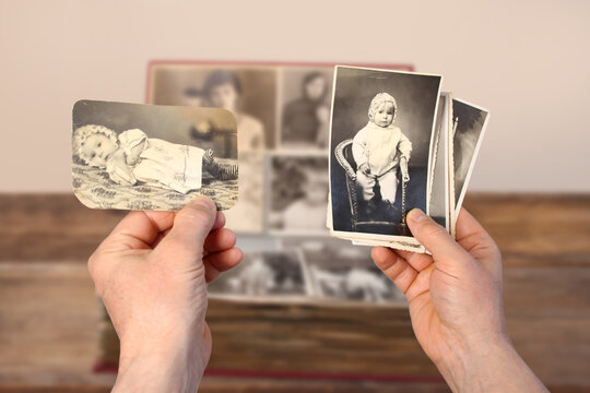 old man’s male hands hold old retro family photos over an album with vintage monochrome photographs in sepia color, genealogy concept, ancestral memory, family ties, childhood memories