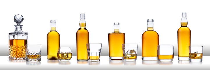 A white bar with a row of bottles of golden whisky, with no label or branding, and glasses of whisky and ice, isolated on white