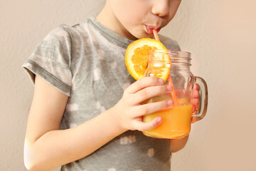 cheerful kid, boy, holds a glass jar in his hand with orange juice from orange or lemon and drinks from a straw, the concept of a healthy diet, vitamins, lifestyle