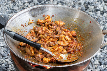 In the pan there is chicken stir-fried with curry. And there was one ladle on top of the charcoal stove,there is a rocky background blur