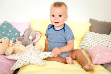 A beautiful little child in a striped vest, sitting in pillows and toys, holding a textile toy starfish, laughing.