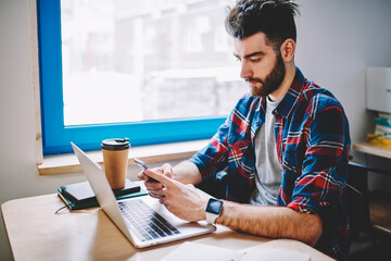 Young man typing sms on cellular during remote work at computer