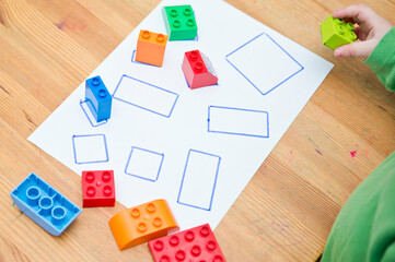 Match to correct shape. Boy placing toy blocks on white paper with defined lines. Toddler education. Early exercise, for preschool children.