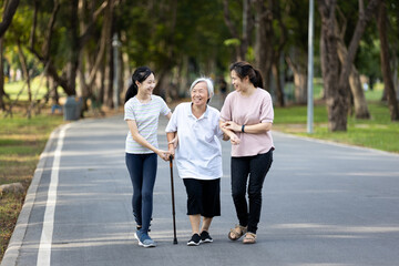 Happy asian family strolling embracing while relaxing and enjoying summer day in city park at leisure,smiling senior grandmother,mother,daughter child walking holding hand together along the promenade