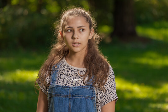 Emotional Teenager Girl With Long Hair In Blue Denim Shorts Walks In The Park On A Sunny Day.