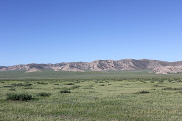 The large, rocky mountains are very gray in the middle of the blue sky, green fields.