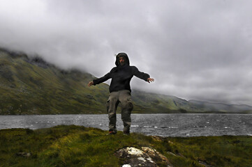 Homme se tenant difficilement debout au bord d'un lac en Irlande, le vent tempétueux et la pluie...