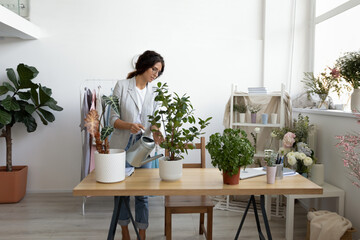 Young Caucasian woman hold pot take care of green plant in office or home fertilize enrich ground,...