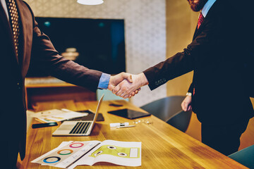 Cropped image of men in suits shaking hands making deal of sponsorship in business corporation, male entrepreneurs agree in partnership cooperation and contract during formal meeting in office - obrazy, fototapety, plakaty