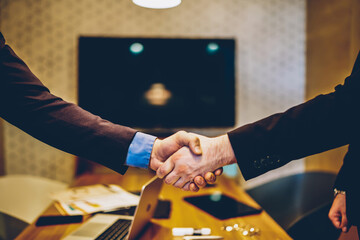 Cropped image of male's hands shaking in sign of making profitable deal for common business project,man agree in strategy of cooperation making contract for partnership in office during meeting - obrazy, fototapety, plakaty