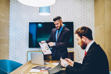 Confident male owner of corporation in suit preparing for making presentation during meeting table in office,prosperous finance director making briefing about incomes explaining strategies to employee