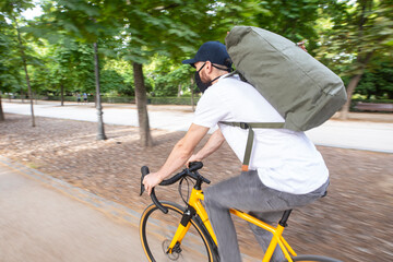 Repartidor de comida a domicilio con mascarilla en bicicleta amarilla por la ciudad con la mochila cargada de pedidos