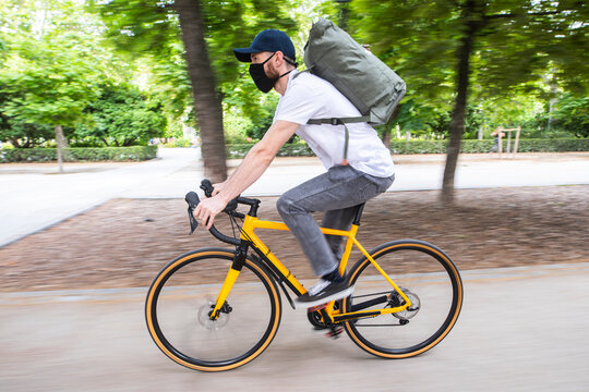 Repartidor de comida a domicilio con mascarilla en bicicleta amarilla por la ciudad con la mochila cargada de pedidos