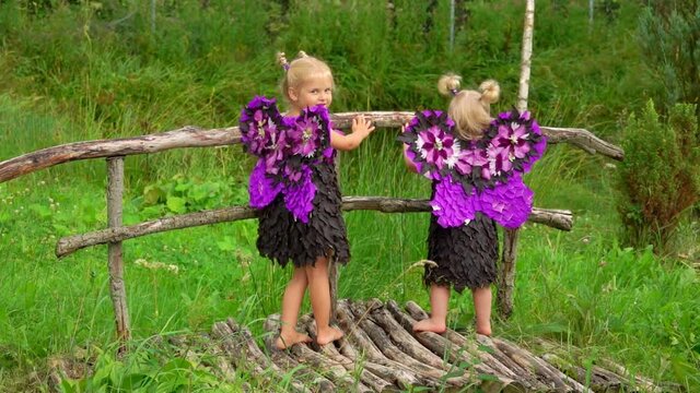 Cute blond girls with purple butterfly wings are standing on the wooden bridge outdoors