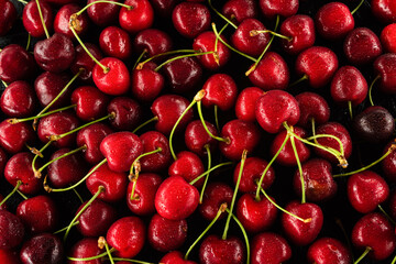 texture of juicy cherries with water droplets and green tails on a black background