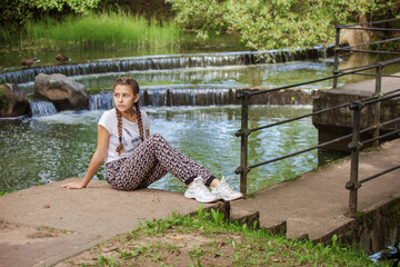 Emotional girl teenager with long hair hairstyle braids walks in the park at the waterfall on a...