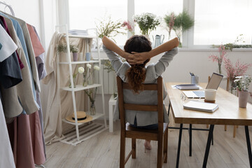 Back view of young female fashion designer relax in chair at workplace look in window distance dreaming or thinking, calm businesswoman enjoy break, relieve negative emotions, stress free concept