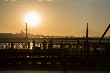 ISTANBUL / TURKEY - 30/05/2015: beautiful contrasty golden hour sunset shot of the Galata Bridge with shadows, silhouettes of people, the Ataturk bridge in the back and a bright yellow sunshine