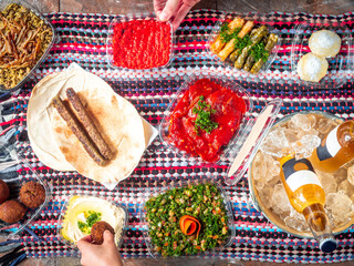 Two People are Sharing a Lebanese Arabic Picnic with Shawarma, Eggplants, Hummus, Tabouleh, Lentil Rice, Kibe, Falafel, Stuffed Vine Leafs and Cold Beers in Ice Bucket