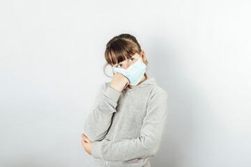 young girl bored by quarantine waits for the new normality at home with a medical mask. White background
